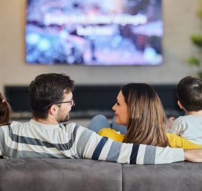 Back view of a family watching TV at home. Rear view of relaxed parents talking while watching TV with their kids on sofa in the living room.
